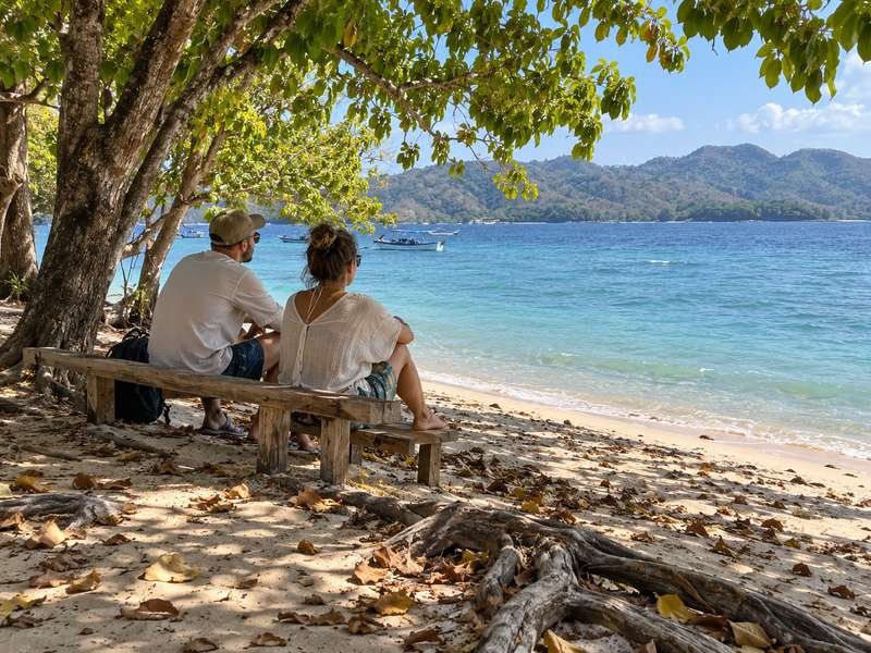 Visitors resting beneath coastal trees on Gili Nanggu